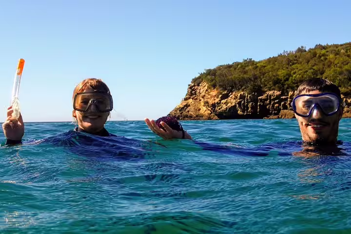 Two snorkelers enjoy clear blue waters near rocky cliffs on an Arrábida snorkeling and wine tour in Portugal.