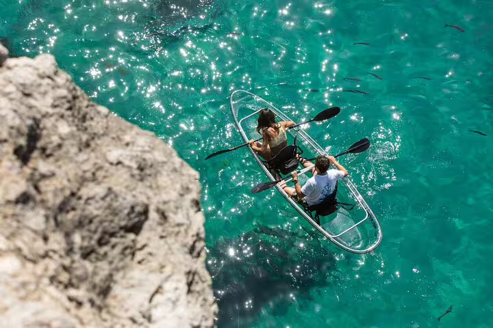 Aerial view of a couple kayaking in a transparent kayak on Arrábida's sparkling turquoise waters, surrounded by fish.