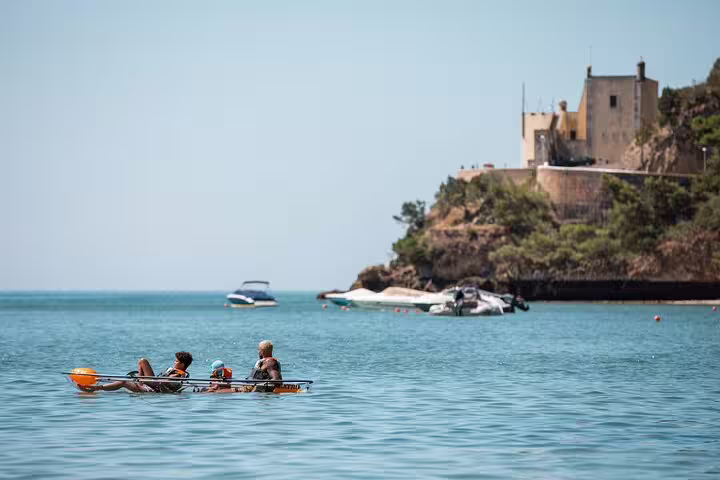 Group enjoying transparent kayaking tour near Arrábida cliffs with serene turquoise waters and historic castle backdrop.