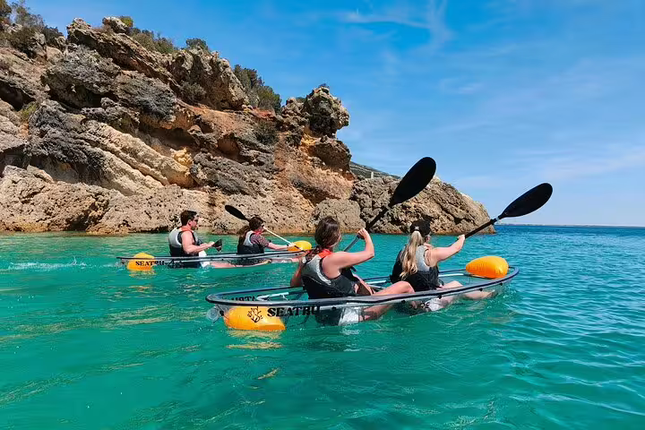 Group enjoying a transparent kayaking tour in Arrábida, paddling near scenic rocky cliffs and clear blue waters.