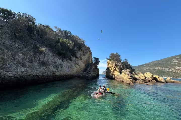 Kayakers navigating through the stunning rock formations and clear waters of Arrábida on a transparent kayaking tour.