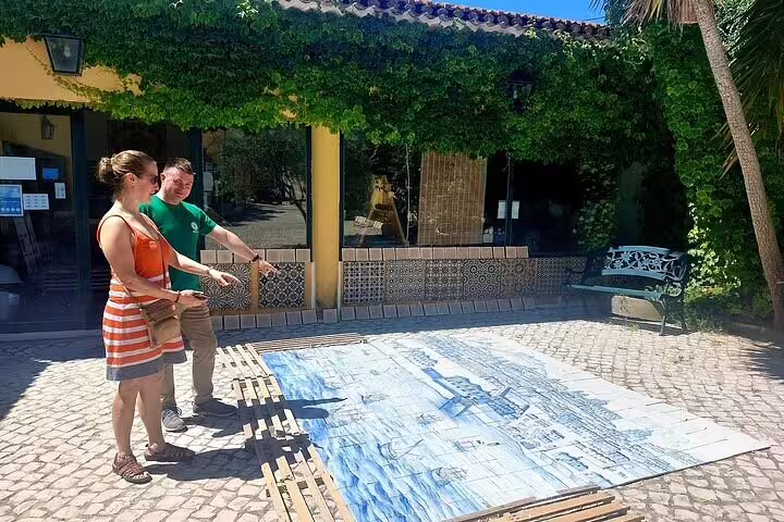 Tourists explore a vibrant courtyard with a large tile mural in Setúbal during the Arrábida Food and Wine Tour from Lisbon.