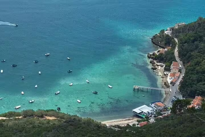Aerial view of the stunning turquoise coastline of Setúbal, highlighting the boats and scenic roads on the Arrábida tour from Lisbon.