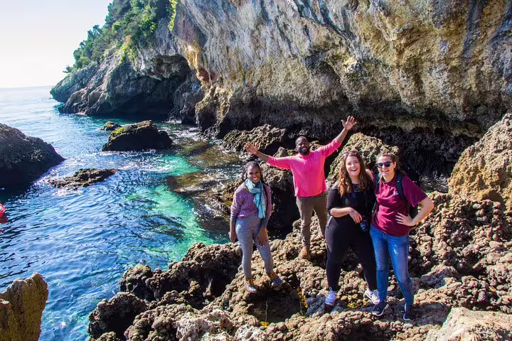 Group exploring stunning Arrábida coast with rocky cliffs and crystal-clear waters, perfect for adventure tours in Portugal.