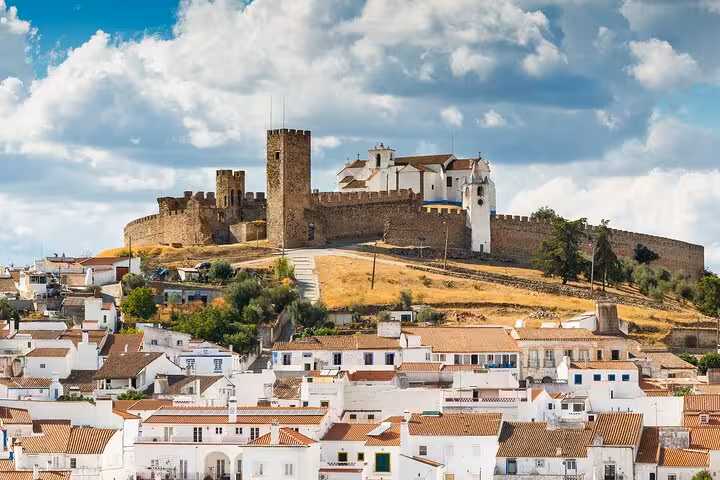 Scenic Arraiolos Castle perched on a hill overlooking whitewashed village houses with dramatic clouds in the background.