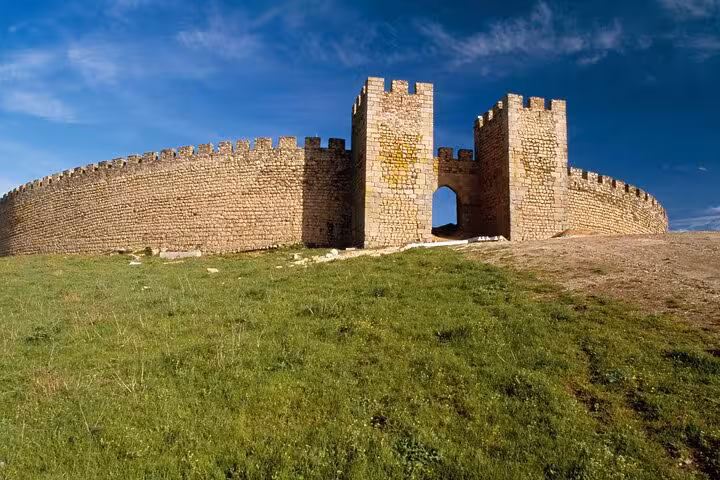 Historic stone walls of Arraiolos Castle against a clear blue sky, highlighting medieval architecture and lush green landscape.