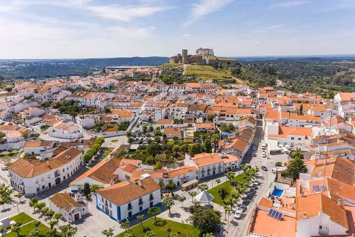 Aerial view of Arraiolos, Portugal, showcasing picturesque white buildings with terracotta roofs and a hilltop castle.
