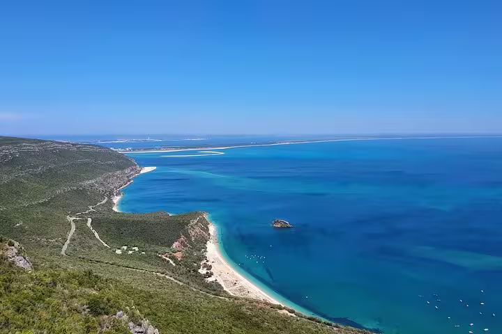 Stunning panoramic view of Arrábida's coastline with clear blue waters and lush green hills on a sunny day.