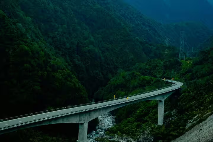 Scenic view of a winding bridge through lush green mountains at Arthur's Pass, perfect for a private alpine vista tour.