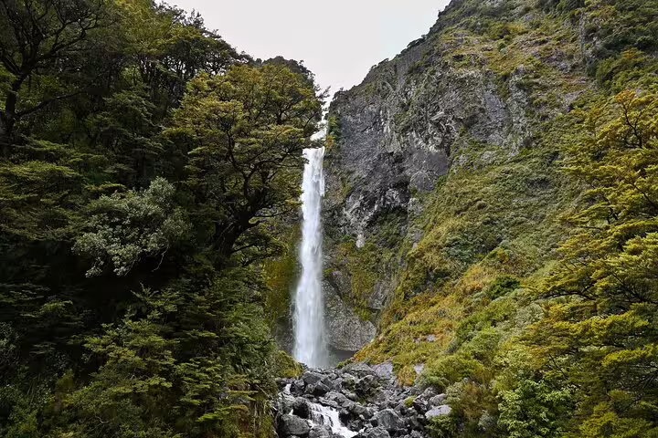 Majestic waterfall cascading through verdant forests and rocky cliffs at Arthur's Pass, ideal for nature exploration tours.