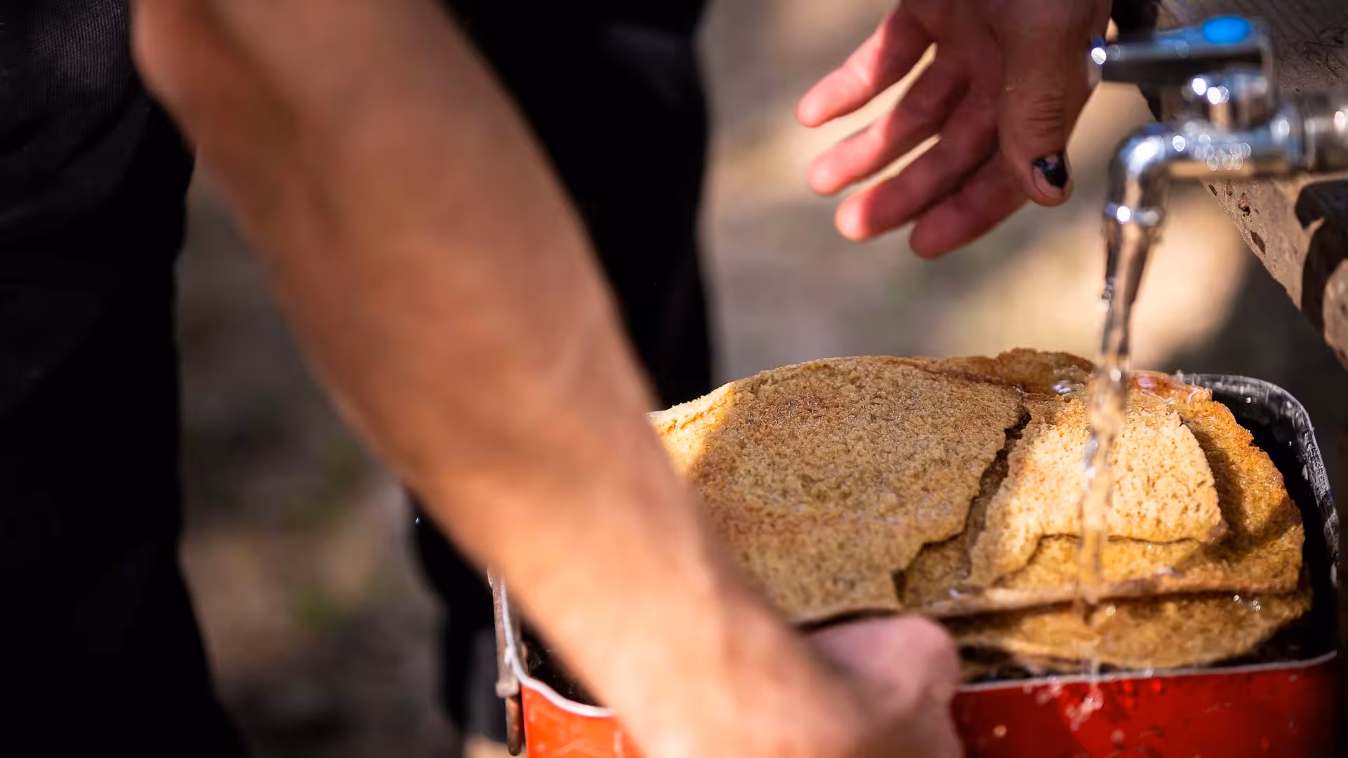 Hands washing traditional Sardinian bread under running water, a glimpse into Arzana farm's culinary experience.
