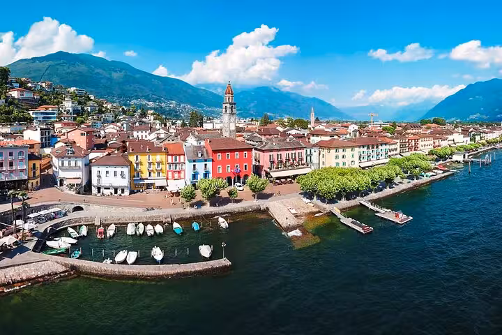 Aerial view of colorful buildings along the lakeside promenade in Ascona, Ticino, with boats docked at Lago Maggiore.