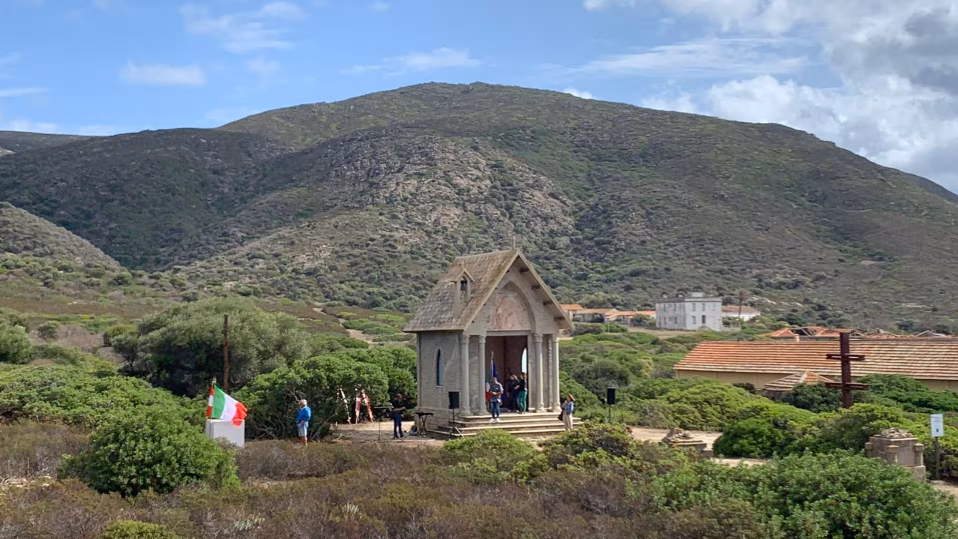 Scenic view of a small chapel surrounded by mountains and greenery on Asinara Island during a guided tour.