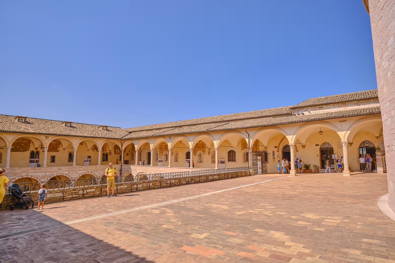 Explore the historic arches of Assisi's courtyard under a clear blue sky in Umbria, ideal for cultural tours.