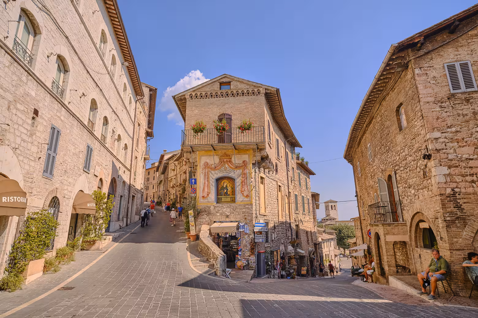Charming street view in Assisi, Umbria, showcasing historic architecture and vibrant local culture on a sunny day.