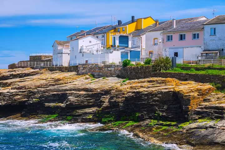 Colorful coastal houses perched on rocky cliffs by the turquoise waters in Asturias, Spain.