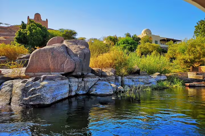Aswan Nile riverbank with granite boulders and lush gardens, view from private day tour to High Dam and Philae