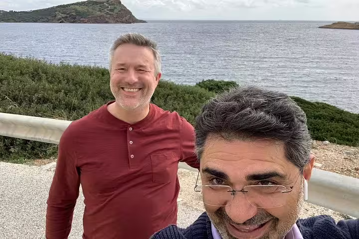 Two smiling tourists enjoy a scenic view of the Aegean Sea during a full-day tour from Athens to Cape Sounion.