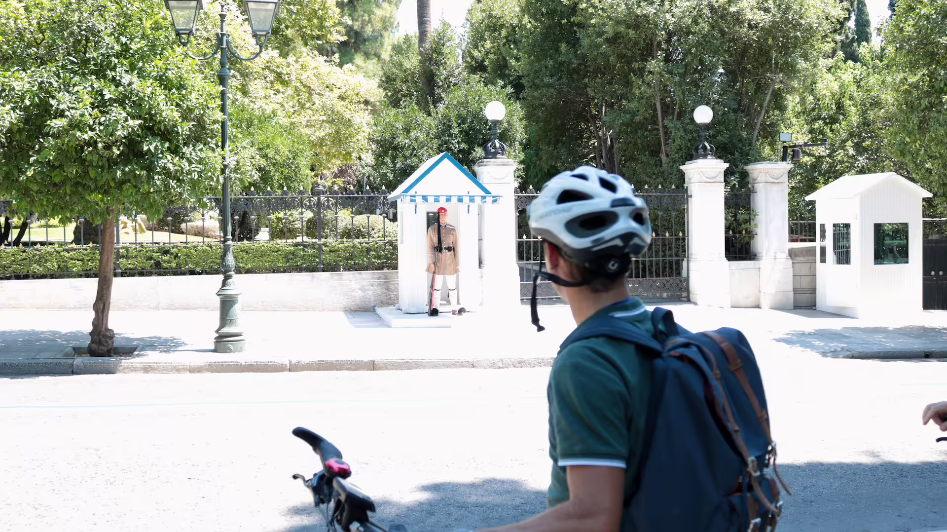 A cyclist observes a traditional guard at a historic site in Athens during an e-bike tour under lush greenery.