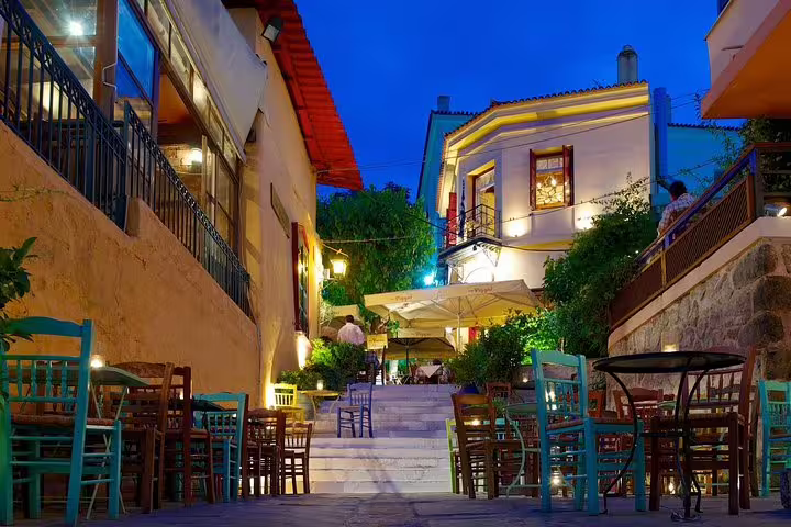 Charming evening ambiance in Athens with lit streets, colorful chairs, and vibrant buildings, perfect for a night sightseeing tour.