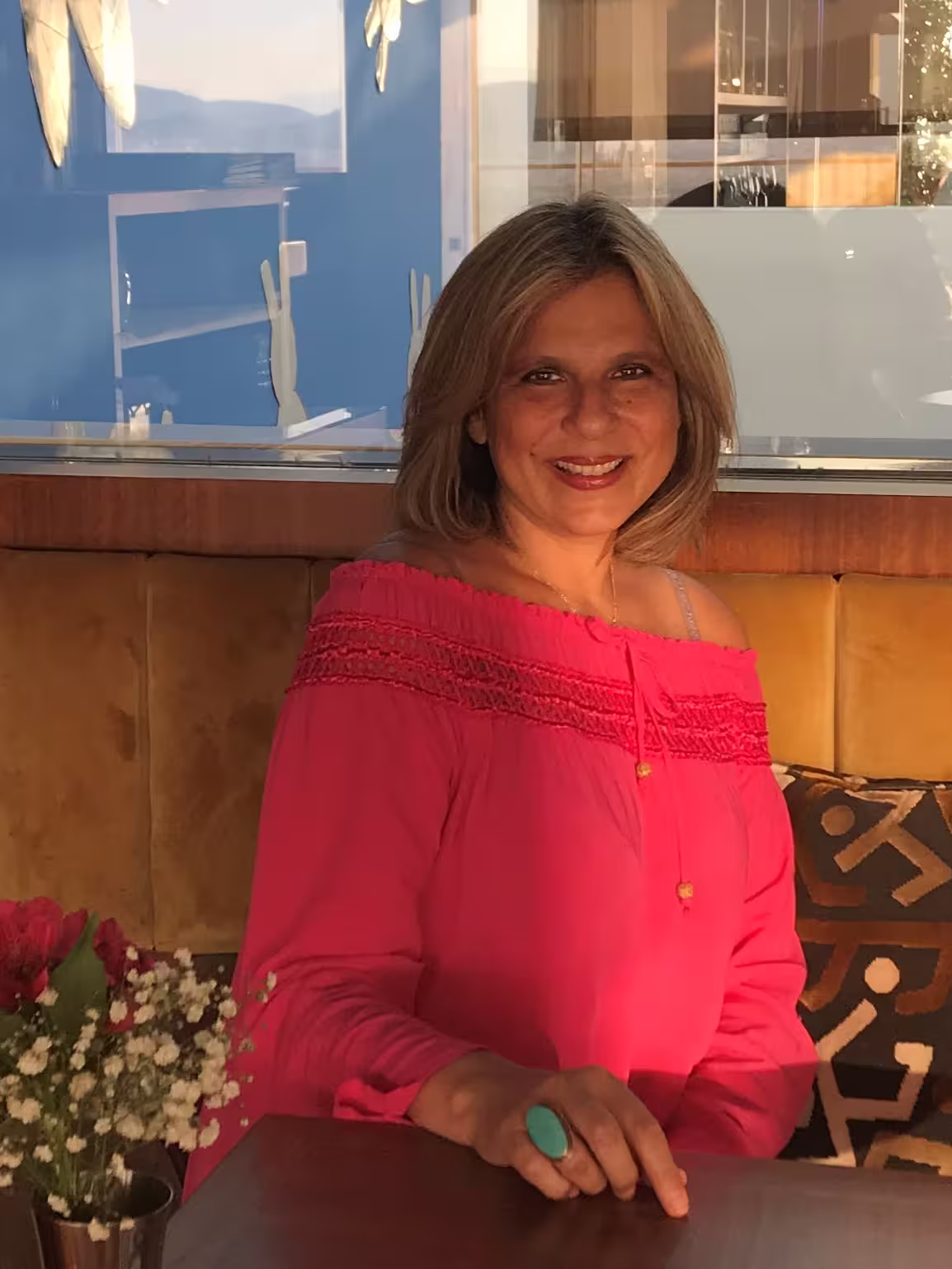Smiling woman in a vibrant pink top enjoys a cozy setting, perfect for an Athens Ancient Greece Symposium Lunch experience.