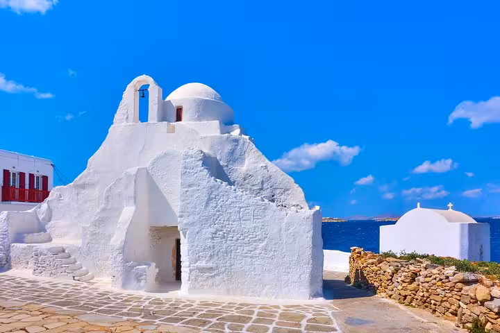 Whitewashed Mykonos chapel by the Aegean Sea under blue sky, featured on the Athens to Mykonos day tour