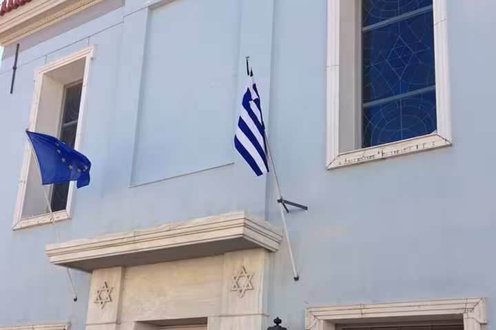 Exterior of a synagogue in Athens with Greek and EU flags, showcasing Jewish heritage architecture.