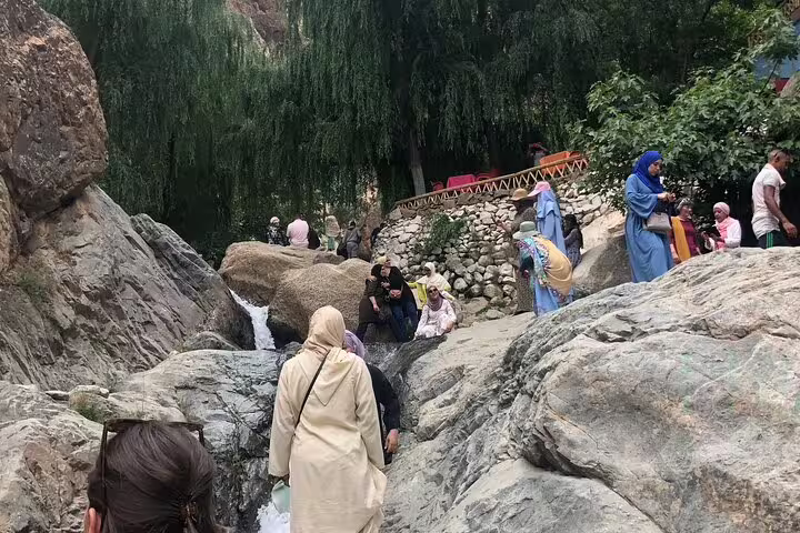 Travelers hiking rocky path by small waterfall in Ourika Valley, Atlas Mountains day trip to Berber villages