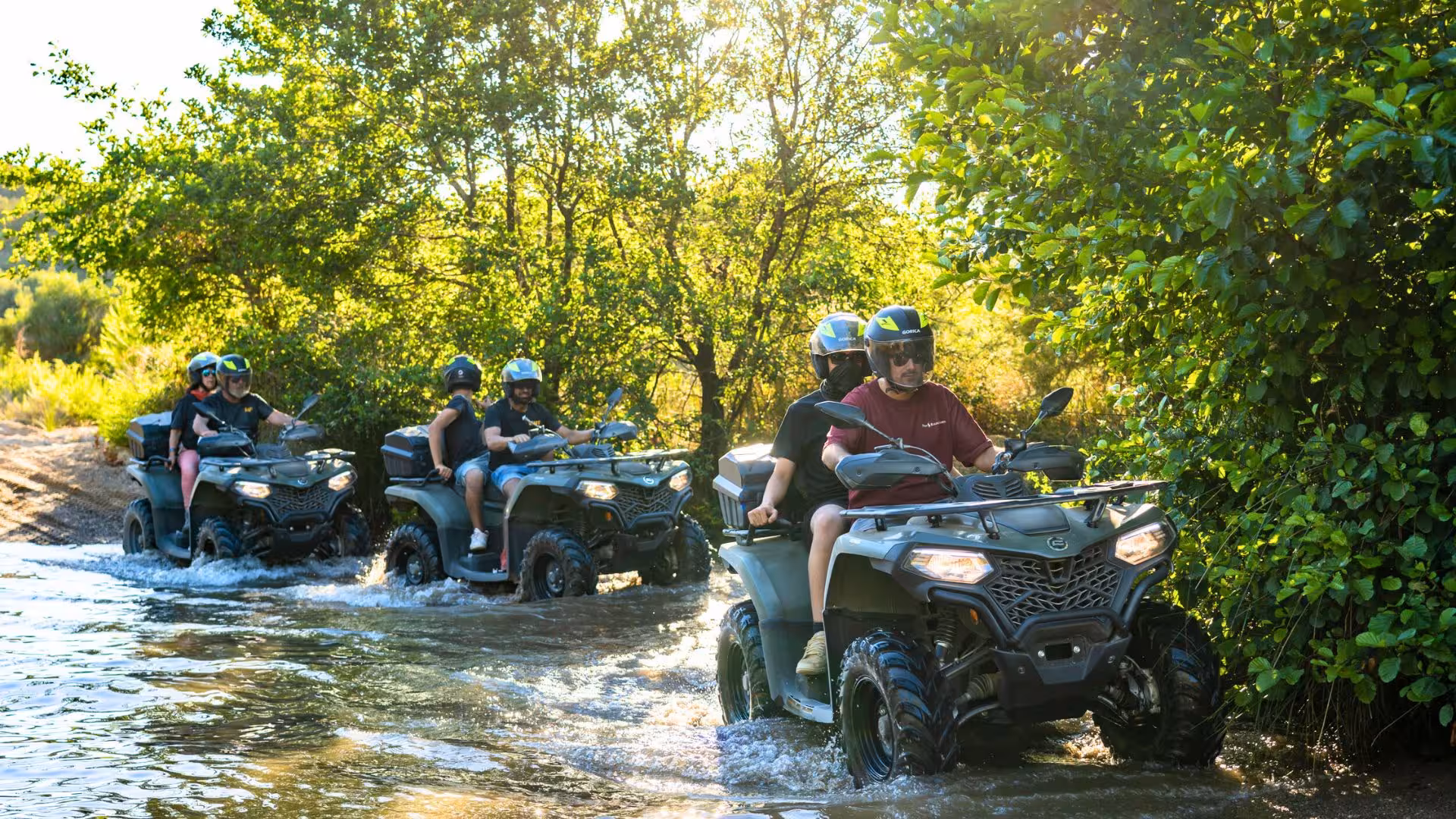 Group of adventurers riding ATVs through a lush, sunlit stream in Costa Verde's scenic landscape.