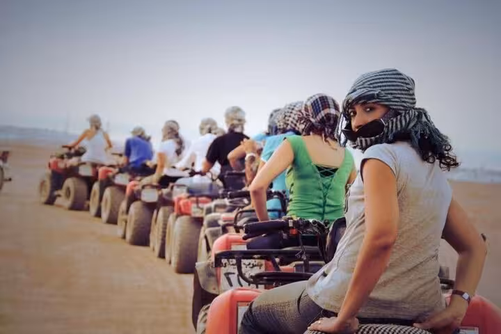 Group of riders on ATV quad bikes in Hurghada desert safari tour, wearing scarves before camel ride
