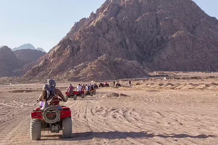 ATV quad bike safari group crossing Marsa Alam desert toward rocky mountains, Egypt off-road adventure