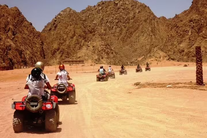 Guided ATV quad bike safari convoy on sandy track in Marsa Alam, Red Sea desert adventure with camel ride