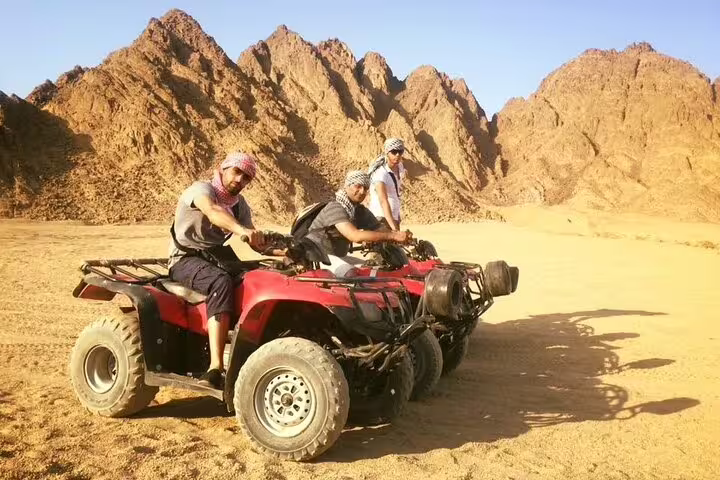 Riders on ATV quad bikes in Marsa Alam desert by rocky mountains, Egypt, on guided quad safari and camel ride