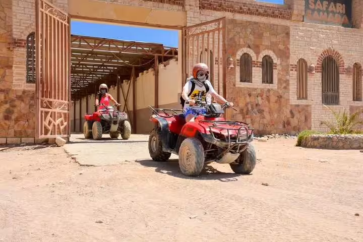 Riders on red ATV quad bikes leaving safari base in Sharm El Sheikh desert adventure tour with camel ride