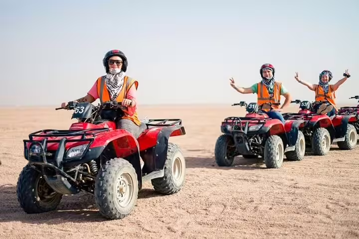 Riders in helmets and scarves on red ATVs during Sharm El Sheikh desert quad bike safari adventure
