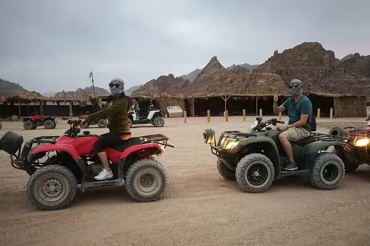 Riders on quad bikes at Sinai desert camp during ATV safari tour from Sharm El Sheikh with mountains behind