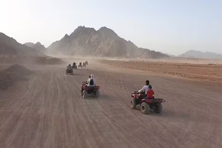 ATV quad bike convoy racing across Hurghada desert plains with mountain backdrop on sunset safari tour
