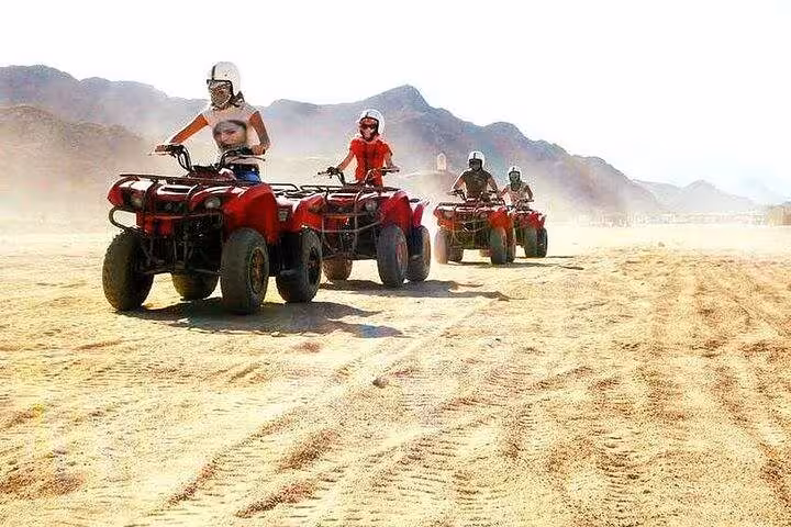 Guided ATV quad bike convoy in Hurghada desert safari, helmets on, speeding over sand with mountains behind