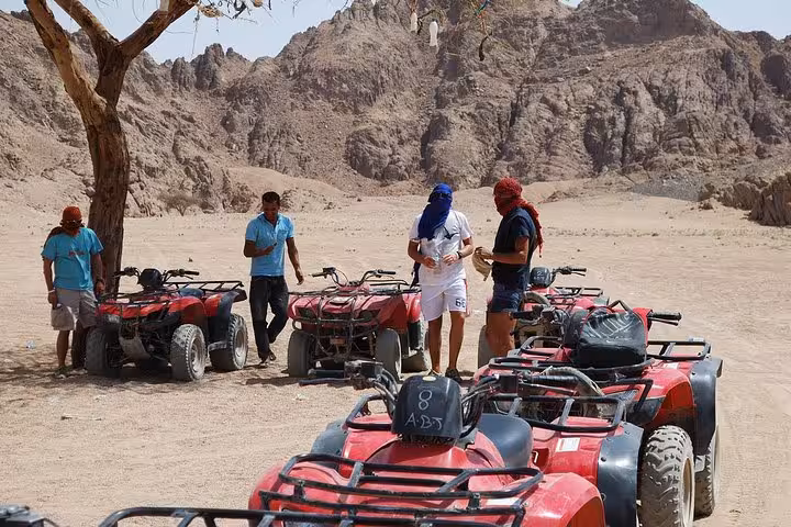 Riders take a break beside red ATVs in Sinai desert mountains on a Sharm El Sheikh quad bike safari