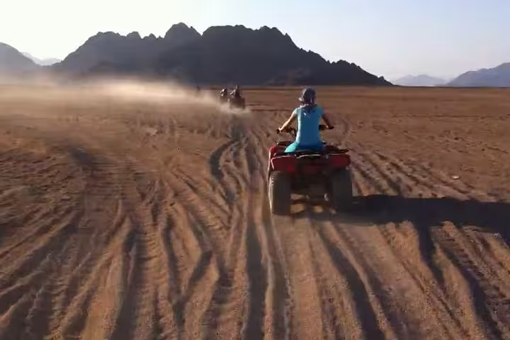 Rider on ATV quad bike safari in Sharm El Sheikh desert, kicking up sand with Sinai mountains ahead