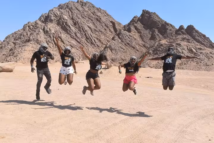 Friends jumping in Sinai desert on ATV quad bike safari in Sharm El Sheikh with rugged mountains backdrop