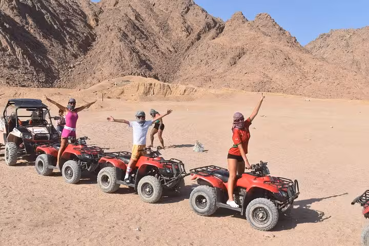 Group riding red quad bikes with guide buggy in Sinai Desert, Sharm El Sheikh ATV safari adventure