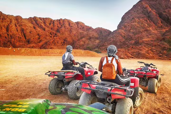 Riders on quad bikes pause at rocky Sinai mountains during ATV safari tour from Sharm El Sheikh at sunset