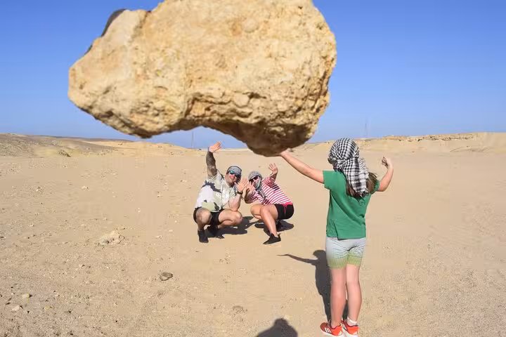 Tourists pose under a huge balanced rock in Sinai Desert on Echo Mountain ATV quad and camel ride tour