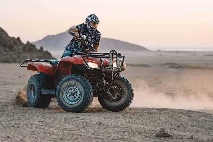 Rider drifting a red ATV quad across Hurghada desert sands, part of a 3-hour quad safari with camel ride