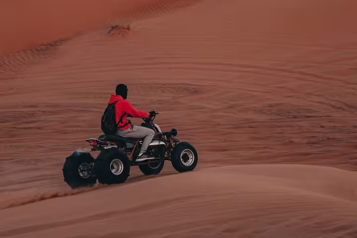 Rider on ATV quad crossing golden dunes in Marsa Alam at sunset, desert safari trip with optional camel ride