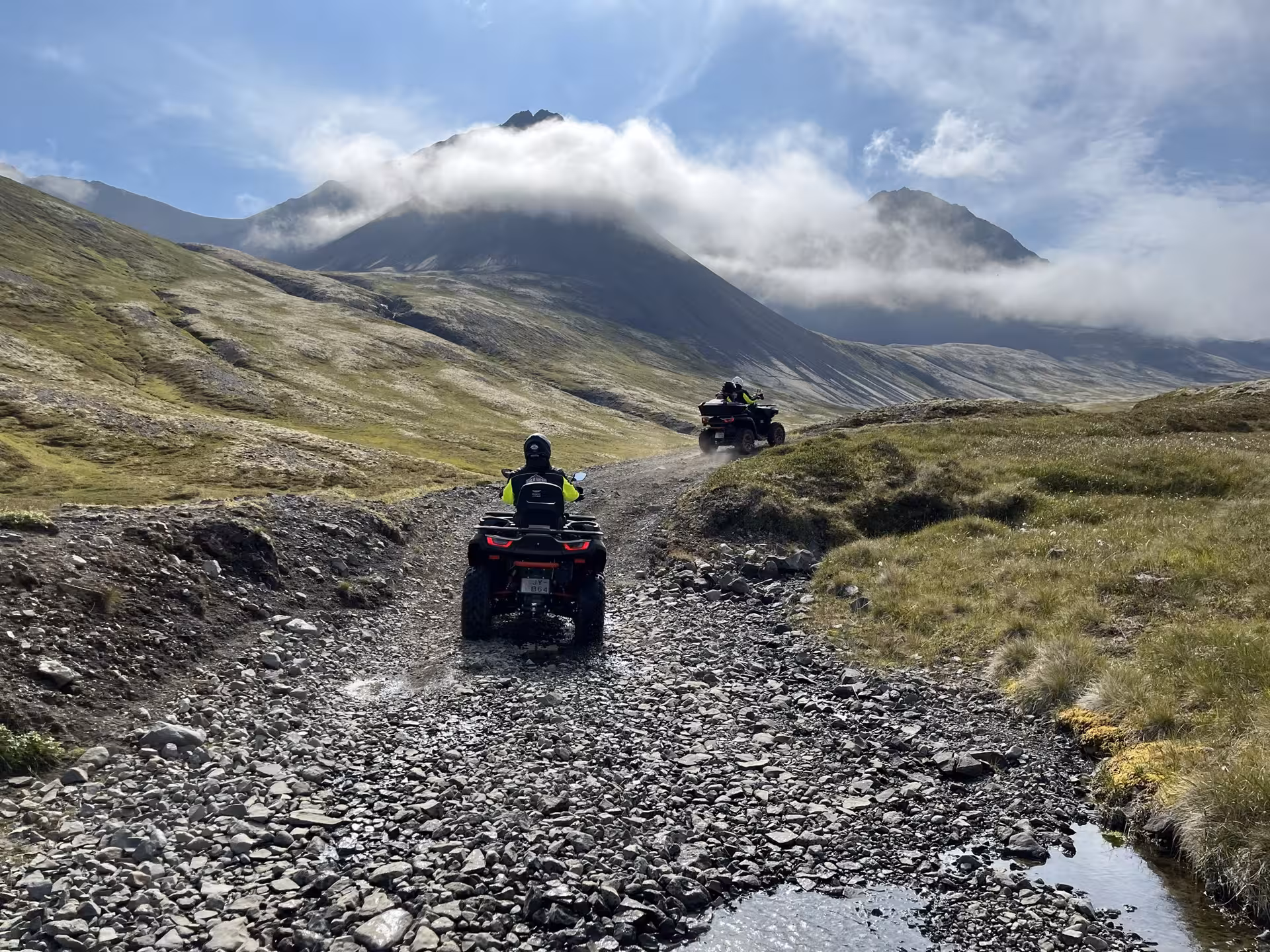 Adventurous ATV riders explore rugged Sléttanes trails against a backdrop of misty mountains and grassy hills.
