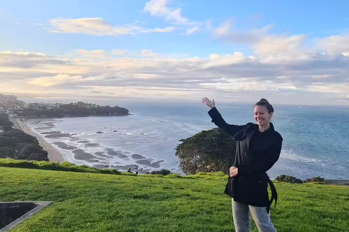 Tourist enjoying a panoramic view of Auckland's coastline, featuring sandy beaches and expansive ocean vistas.