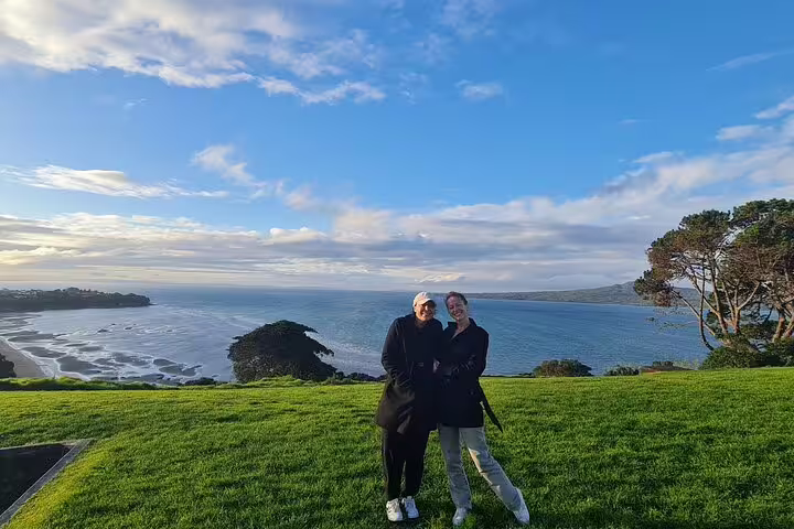 Two people standing on a grassy hill with a stunning view of Auckland's coastline and ocean, perfect for sightseeing.