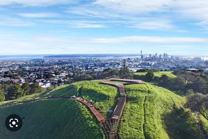 Panoramic view from Mount Eden overlooking lush greenery and the Auckland cityscape.